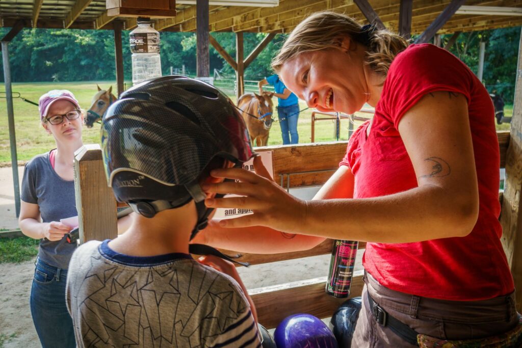 Graduate student helps a camper with his helmet.